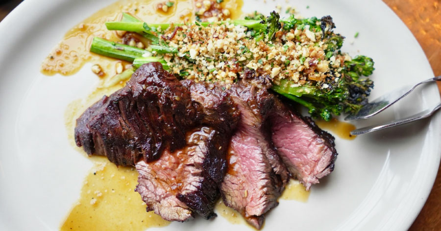 Close-up view of a white plate with a sliced medium-rare steak and a side of broccoli with a nutty sauce.