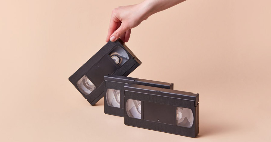 A hand is holding the edge of a VHS tape beside two other VHS tapes, an outdated technology and an easy item to declutter before moving.