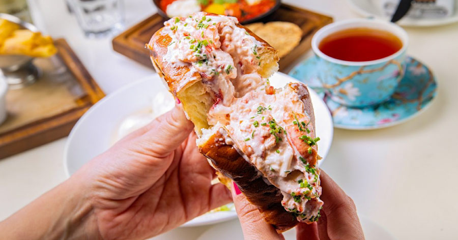 Close-up of hands holding a delicious-looking lobster roll, like those found at some of the best restaurants in Boston.