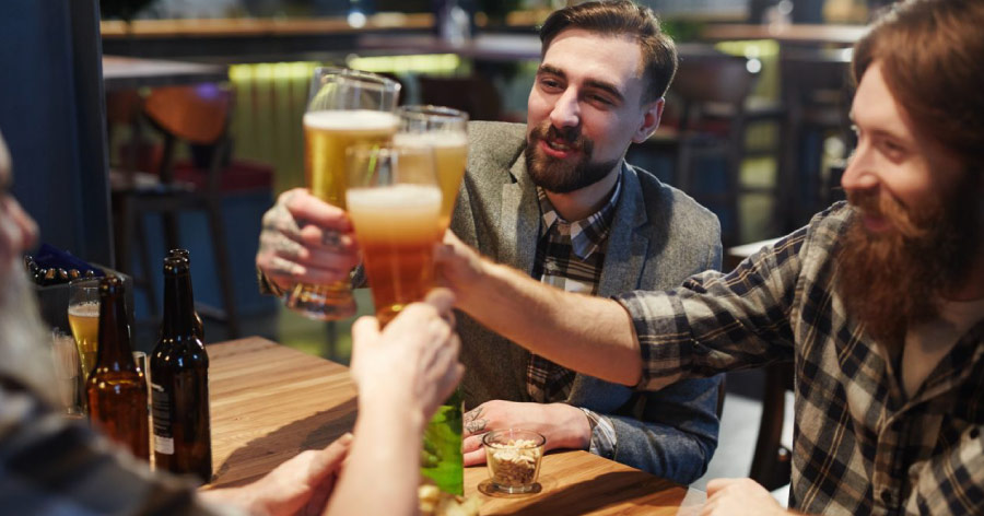 Three happy men clink their beer glasses together at a gastropub while dining out.