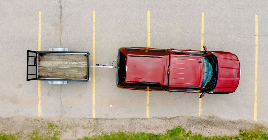 Top-down view of a red truck with a trailer hooked up, parked across four spaces in a parking lot.