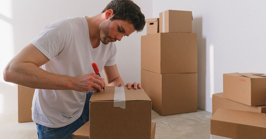 A man labels cardboard moving boxes with a marker to keep household belongings organized for easier packing and unpacking.
