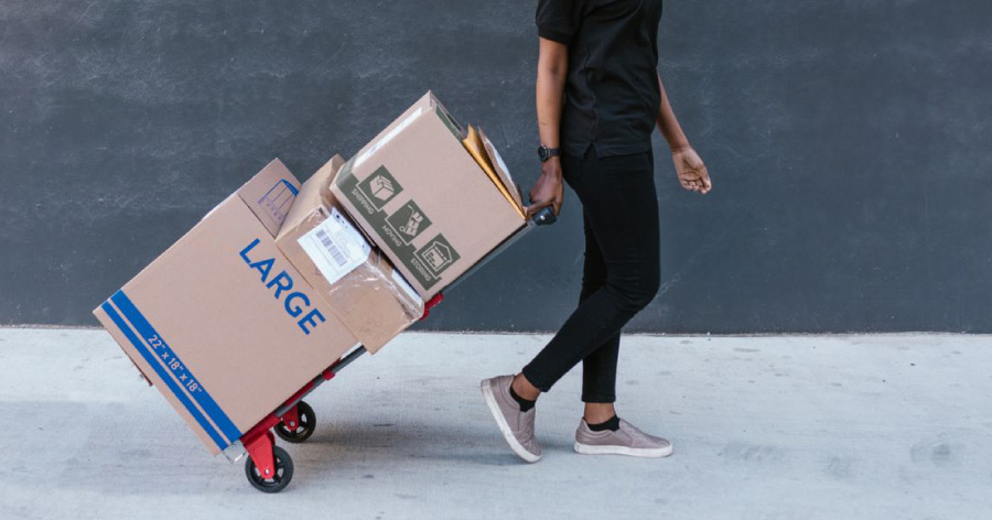 A woman is pulling a dolly loaded with three storage boxes, ready to be put in storage.