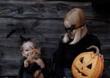 Mother and daughter in matching halloween costumes, holding a jackolantern