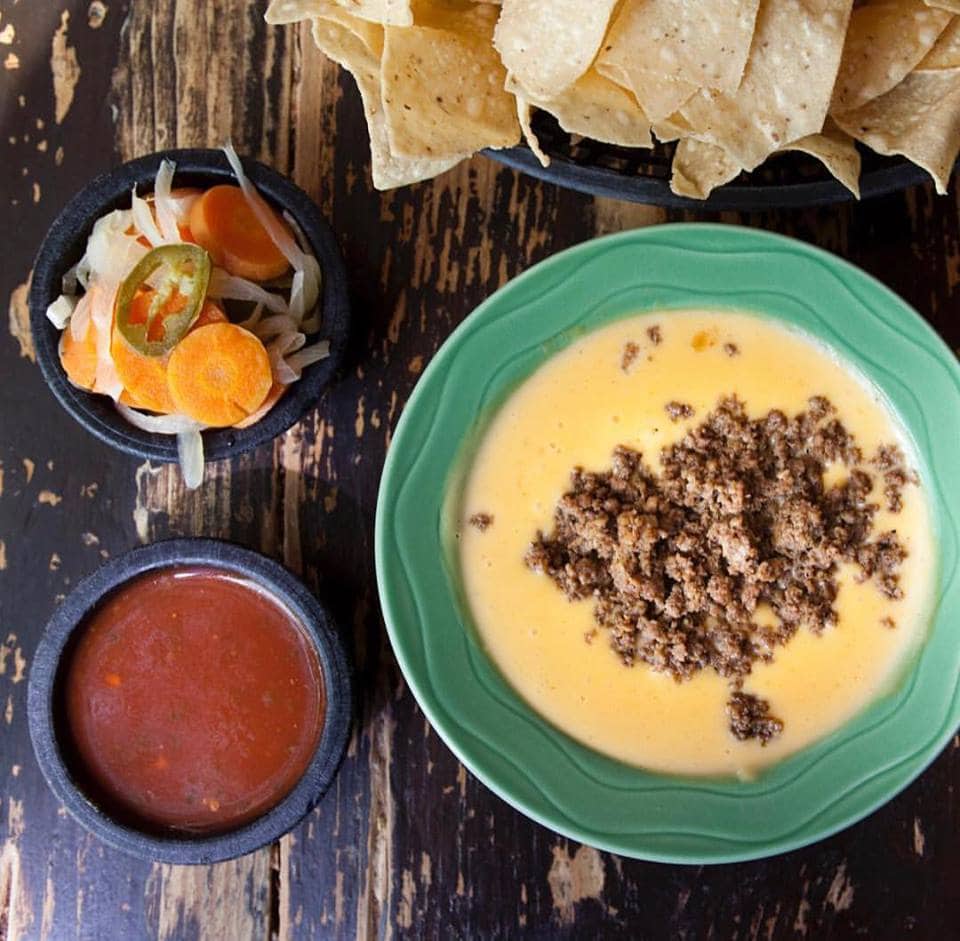 table with chips, salsa, and a bowl of chili con queso topped with taco meat