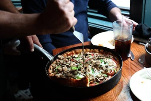 person cutting into deep dish pizza at table