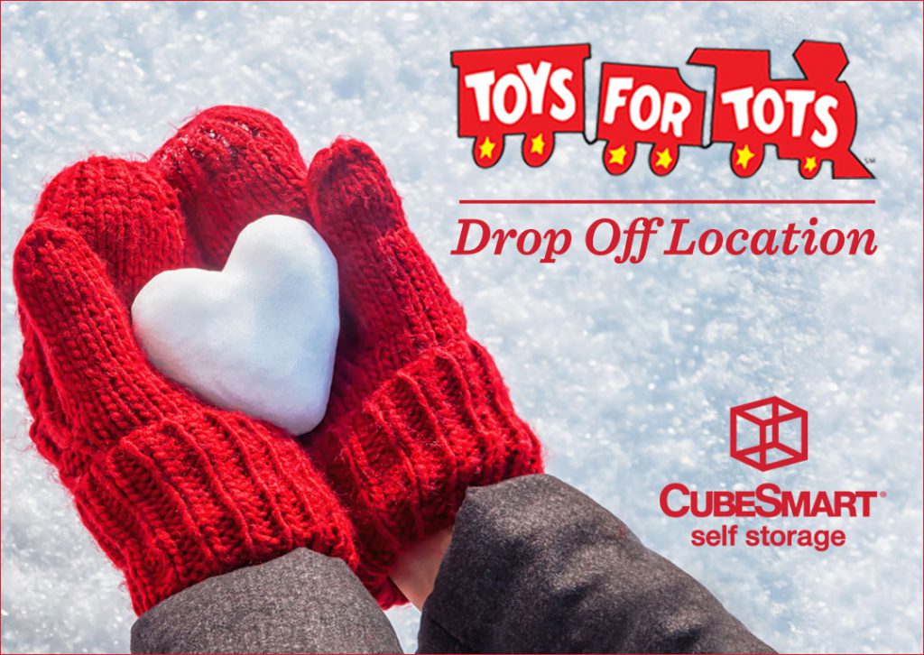 Gloves holding a heart made of snow with the Toys for tots logo.