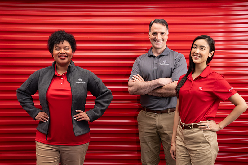 Three Cubesmart store teammates standing in front of a large red storage door.